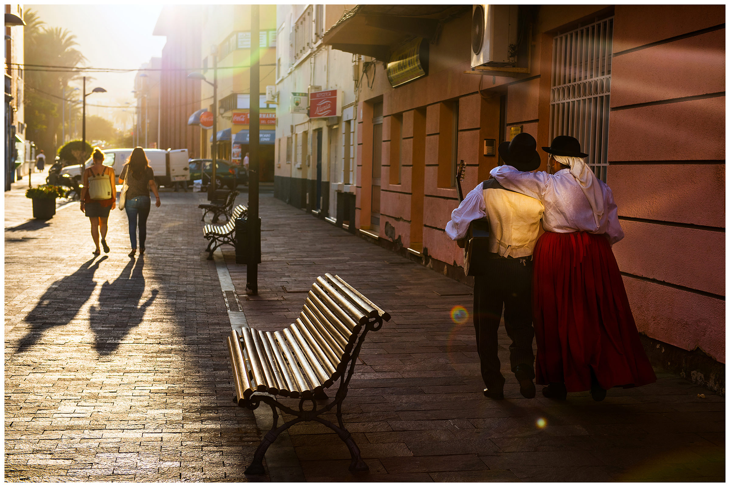 San Sebastian de la Gomera, La Gomera, Canary Islands, Spain. The inhabitants of the city of San Sebastian de la Gomera celebrate the city festival Romeria. A man with a guitar and a woman go hugging in the back light at sunset.