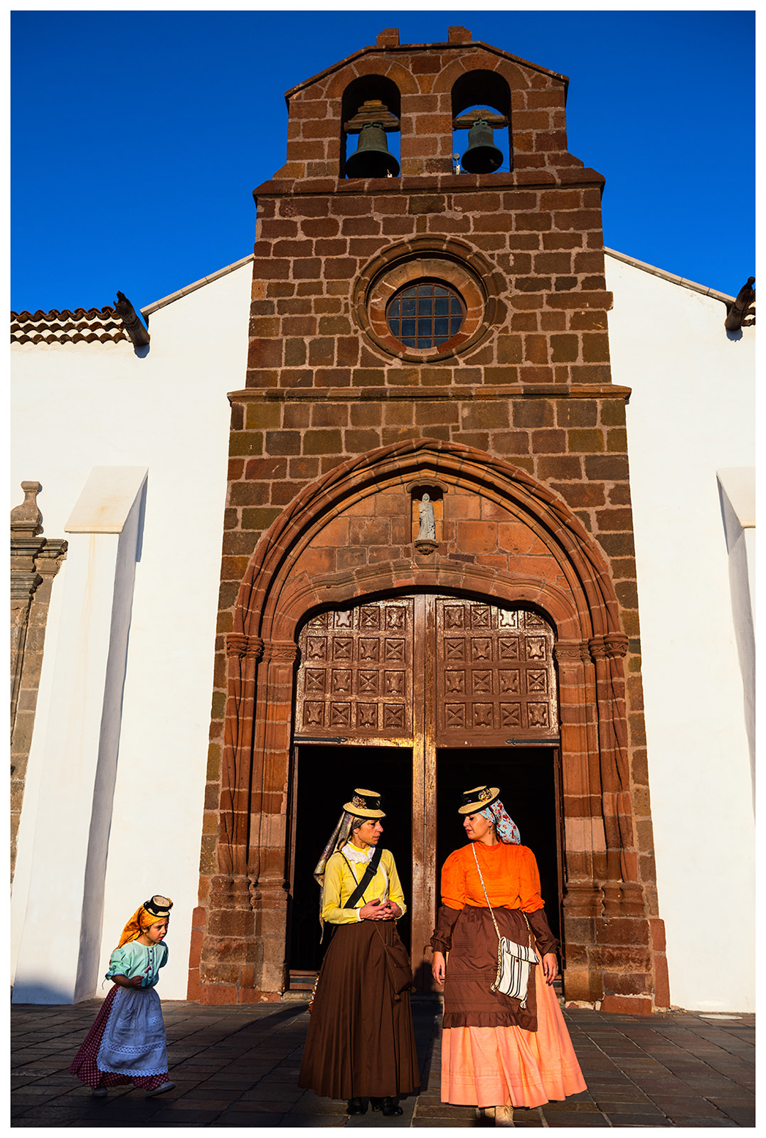 San Sebastian de la Gomera, La Gomera, Canary Islands, Spain. The inhabitants of the city of San Sebastian de la Gomera celebrate the city festival Romeria. Two women and a girl come out of a church.