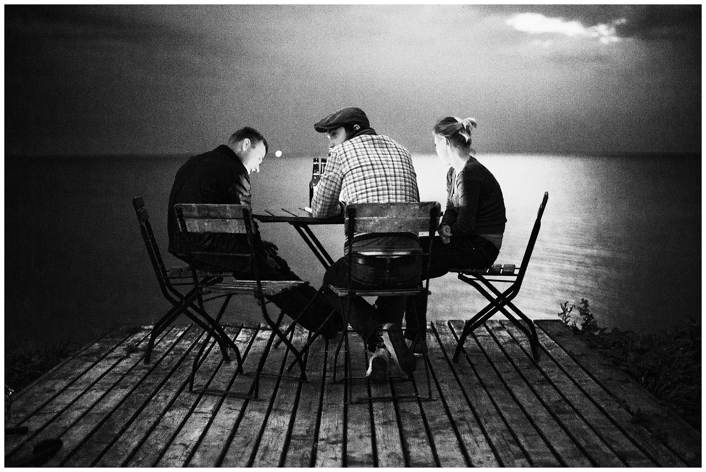 Kaliningrad, Russia. Two men and a woman sit at a table on the coast at night.