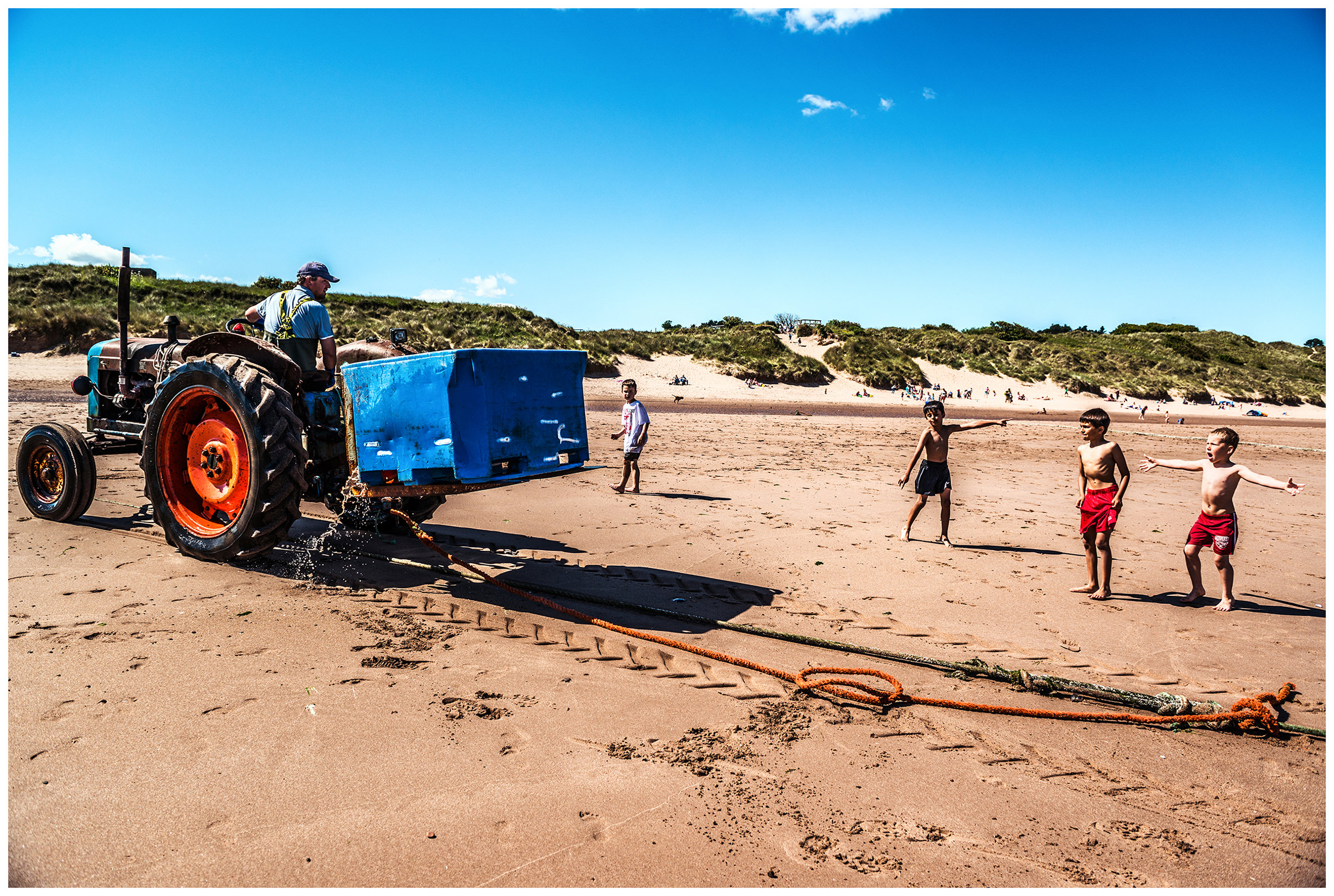 Scotland, Usan Montrose. A man repairs fishing nets with a tractor and children on the seashore greet him.