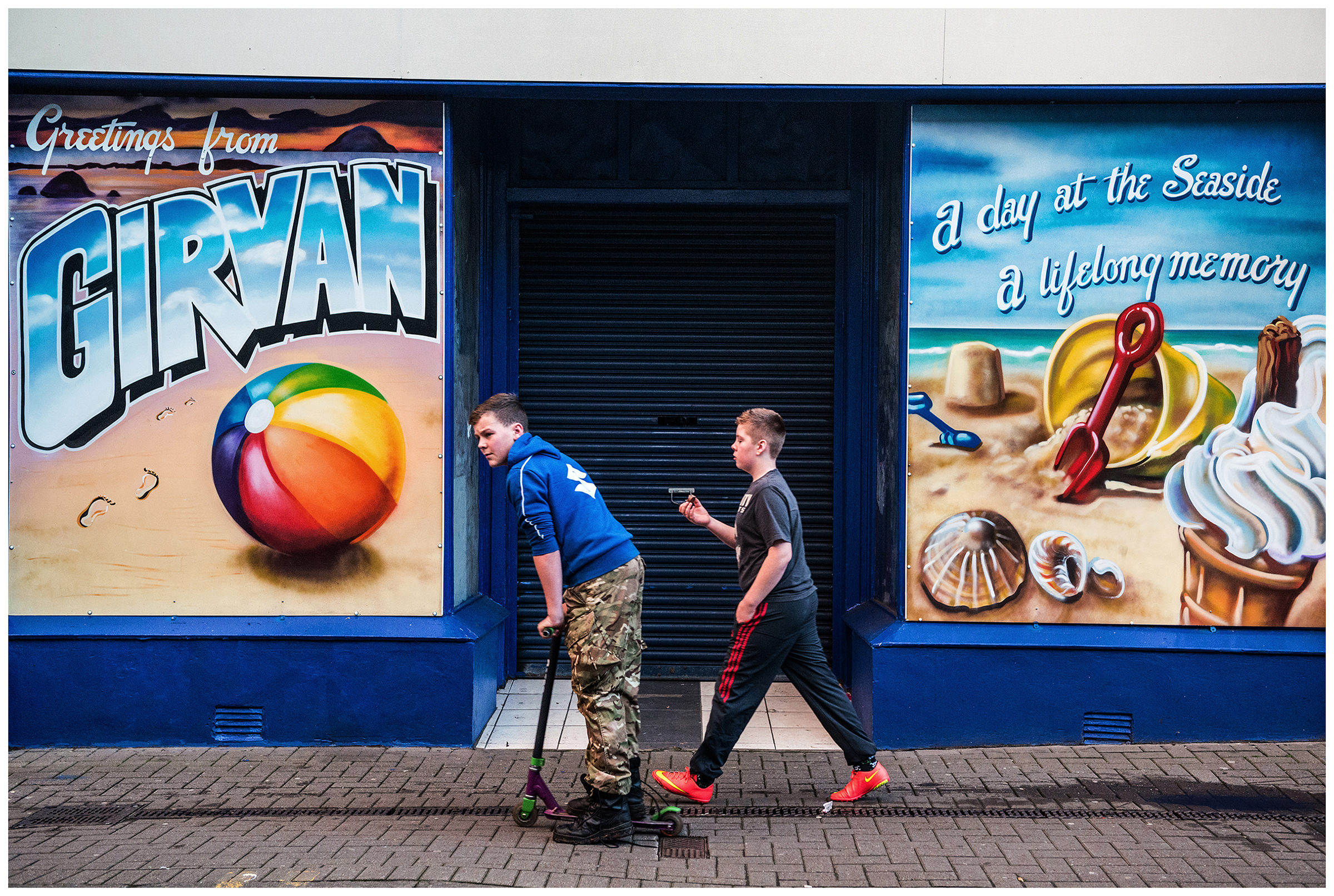 Scotland, Girvan, Ayrshire. Two boys pass a city advertisement.