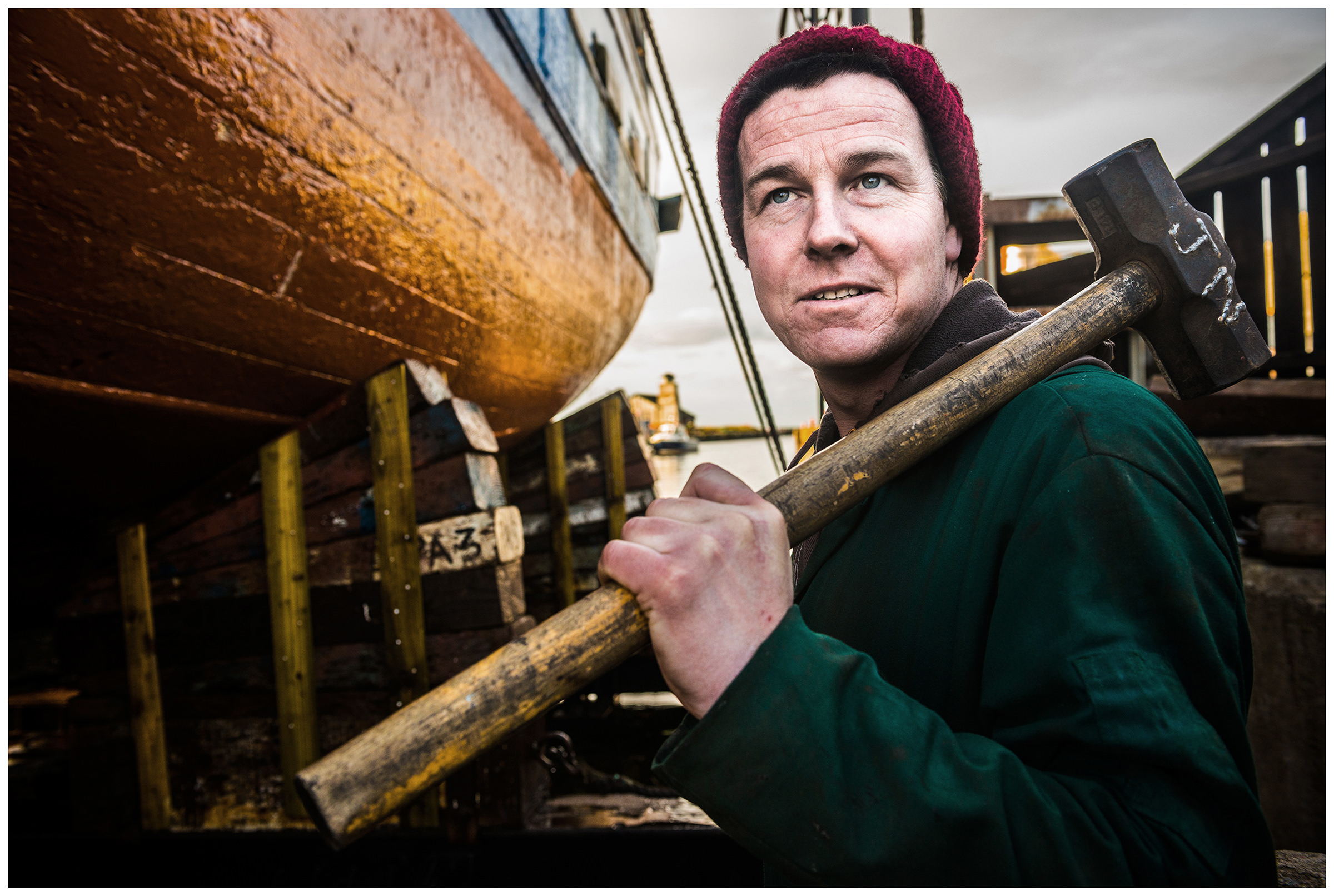 Scotland, Peterhead. A man with a hammer on his shoulder stands in front of a ship.
