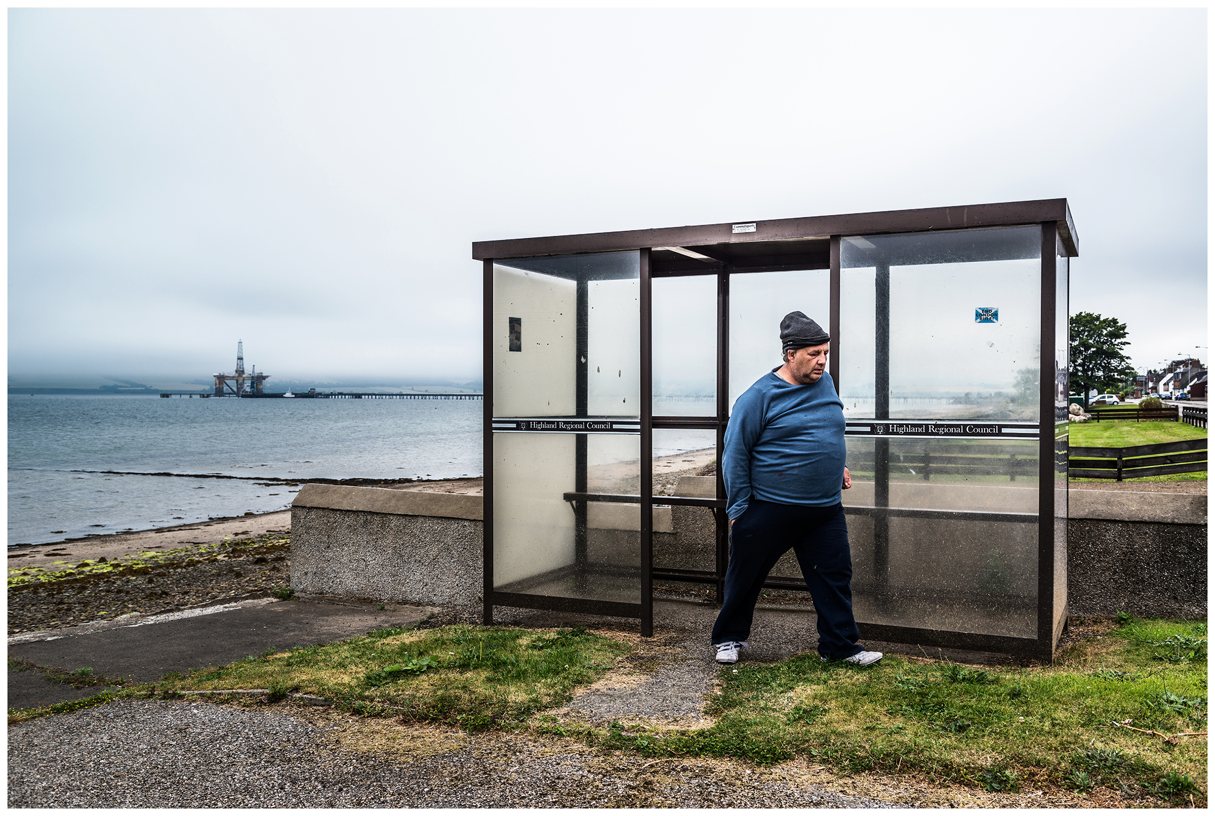 Scotland, Invergordon. A man stands at a bus stop in Invergordon.