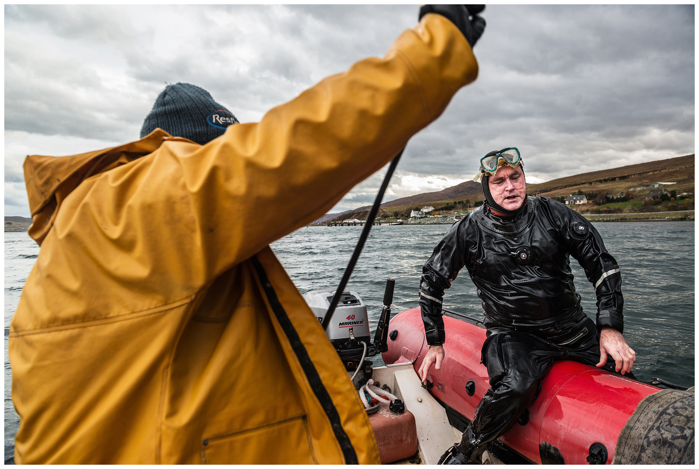 Scotland, Isle of Skye, Sconser. A scallop collector in a diving suit comes aboard a boat.