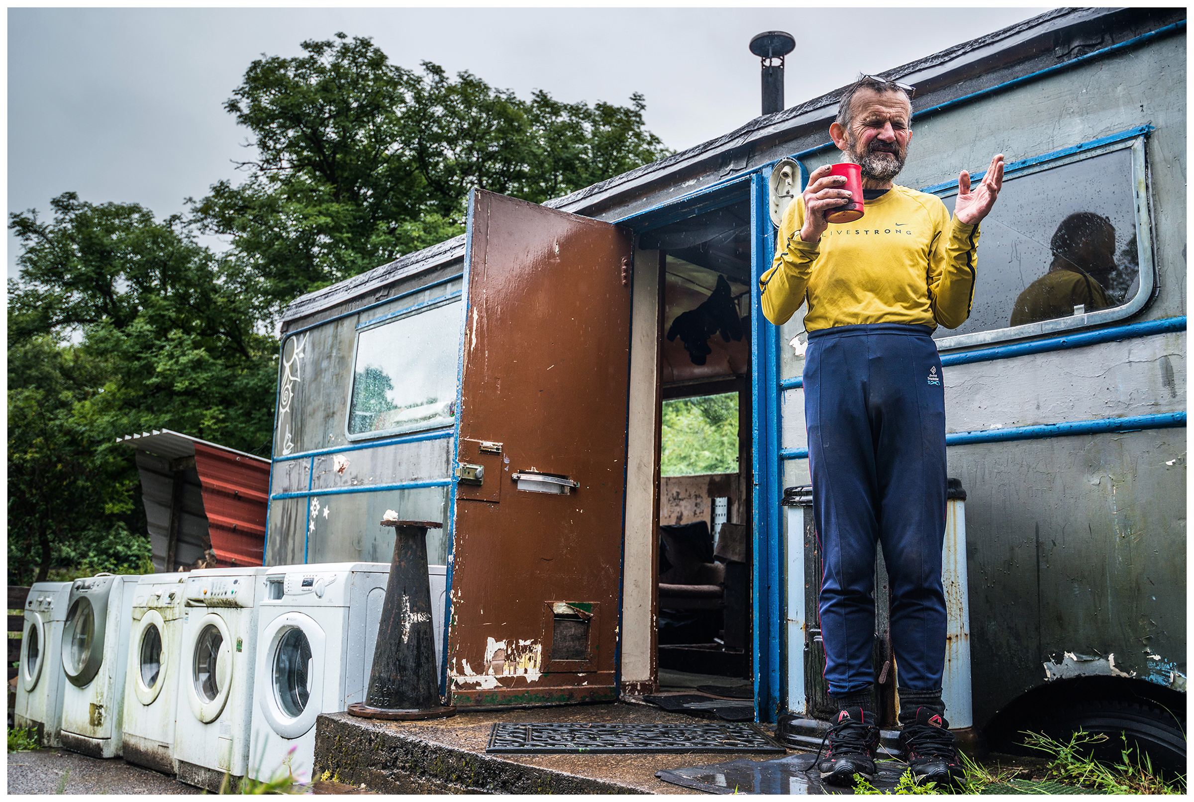 Scotland, Fort William An old man stands in front of his living container and five washing machines.
