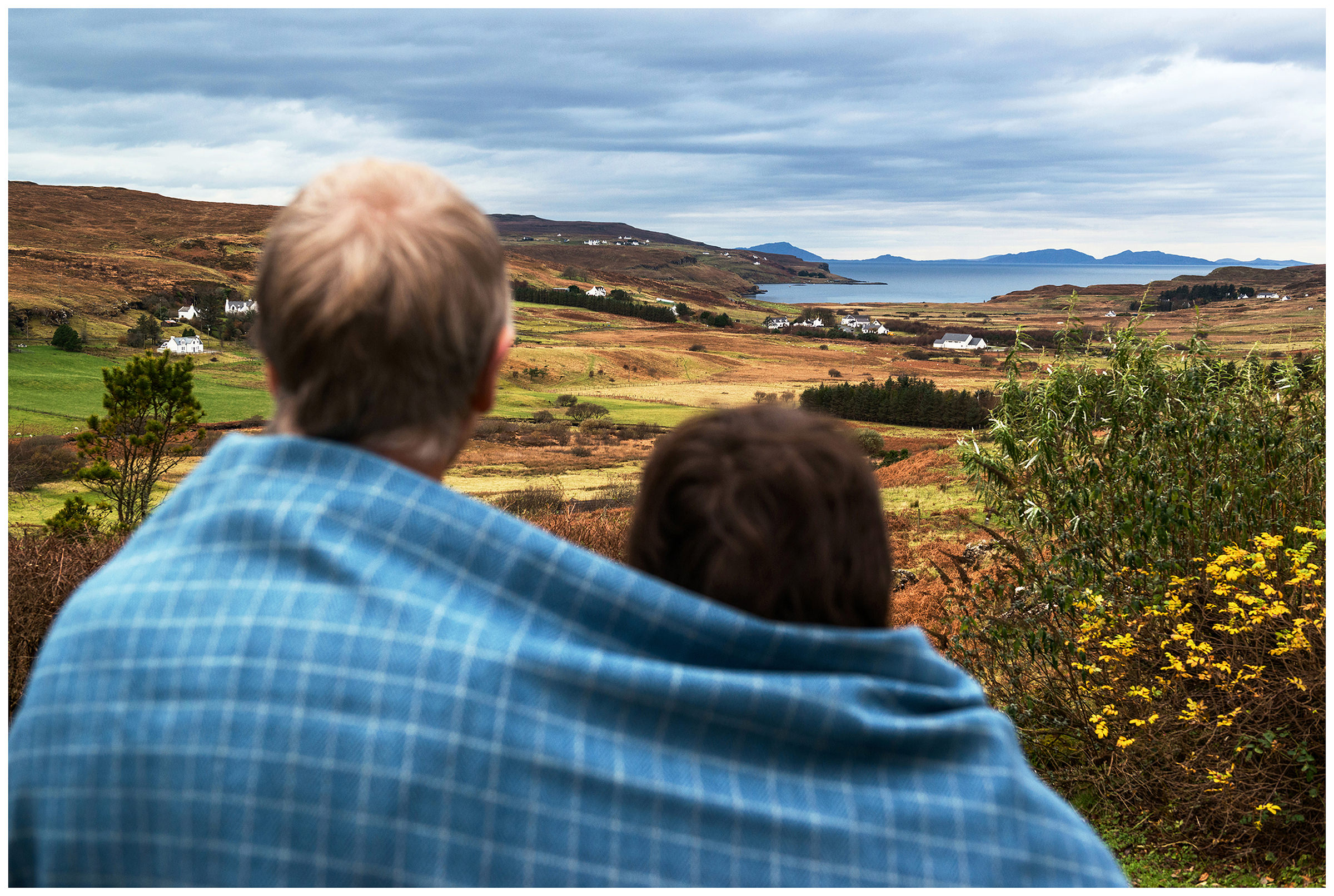 Scotland, Isle of Skye. Two weavers, a man and his wife, are standing near their weaving mill, wrapped in tweed made by them.