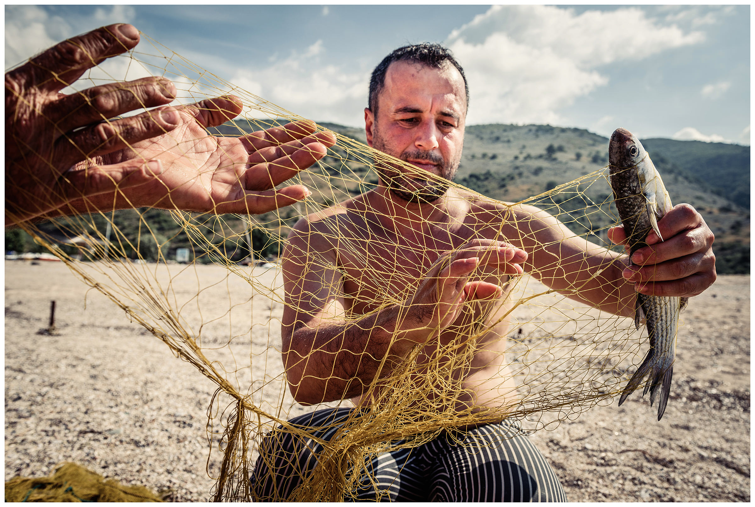 Albania, Jale. A fisherman is pulling his catch out of the fishing net at the coast.