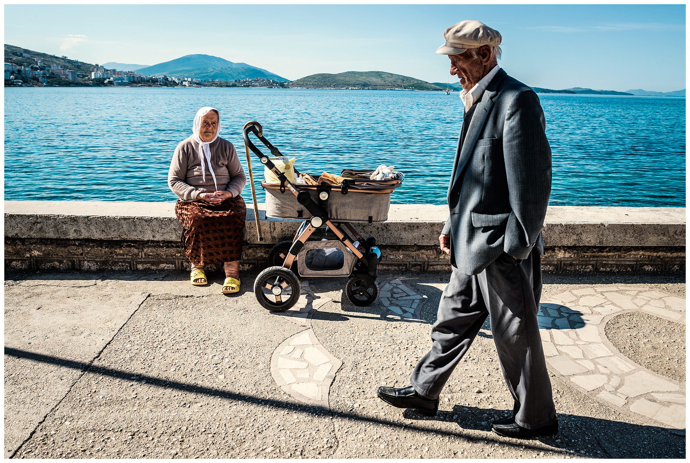 Albania, Saranda. An old man walks past an old woman with a pram on the promenade of Saranda.