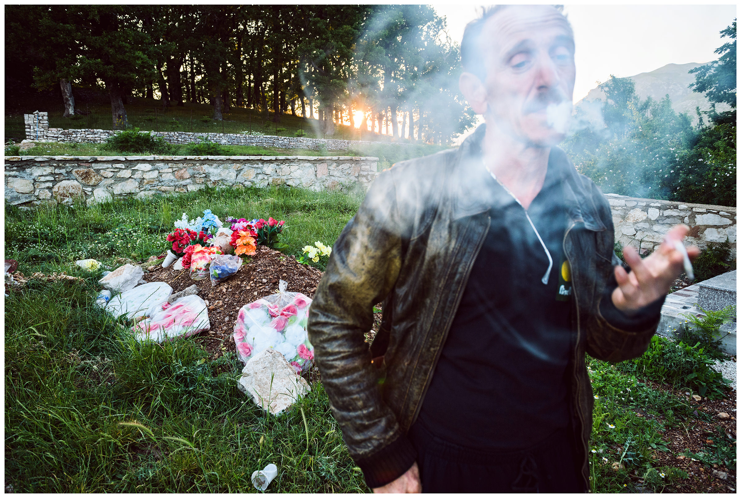 Albania, Pilur. A man smokes at the grave of his recently deceased brother in the village cemetery.