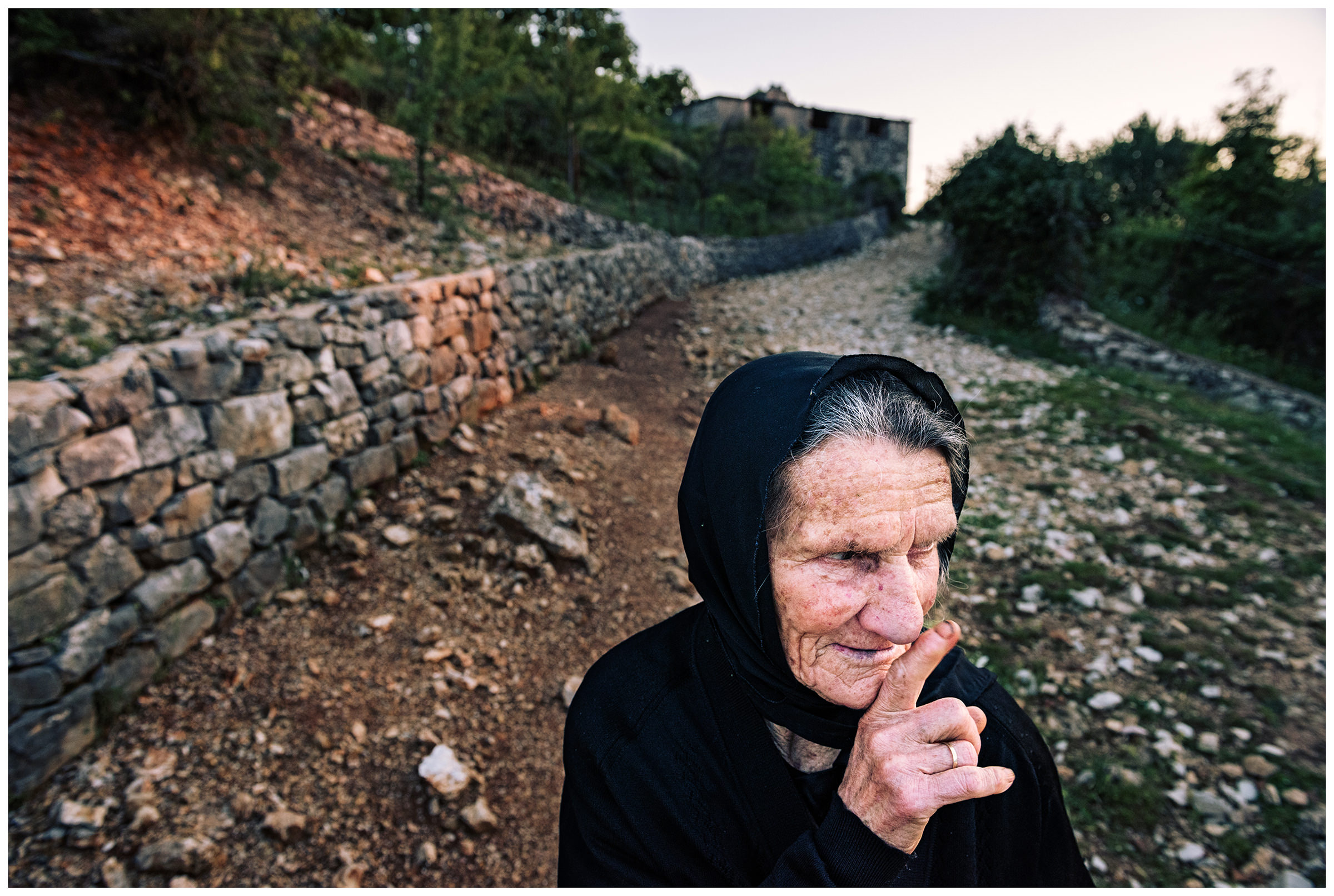 Albania, Pilur. An old woman walks down a village street.