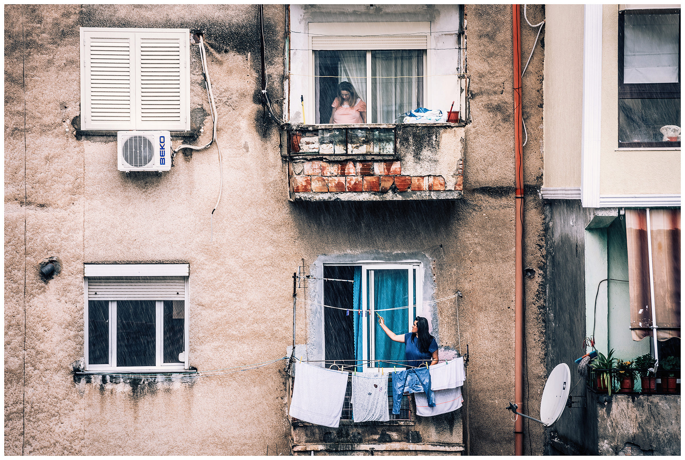 Albania, Tirana. A woman fetches her laundry hanging outside to protect her from showers.