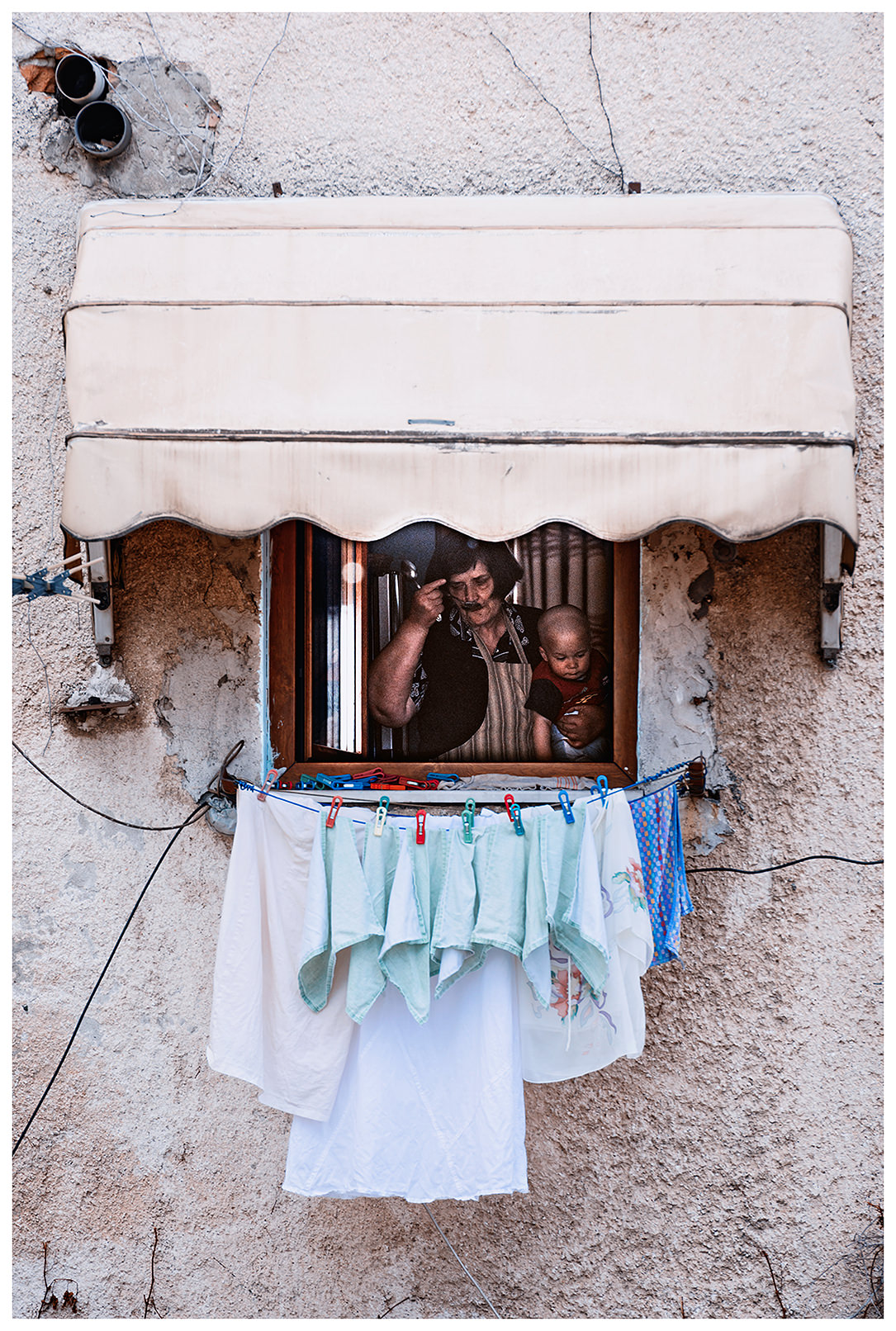 Albania, Tirana. A woman stands with a baby at her home in front of the open window.