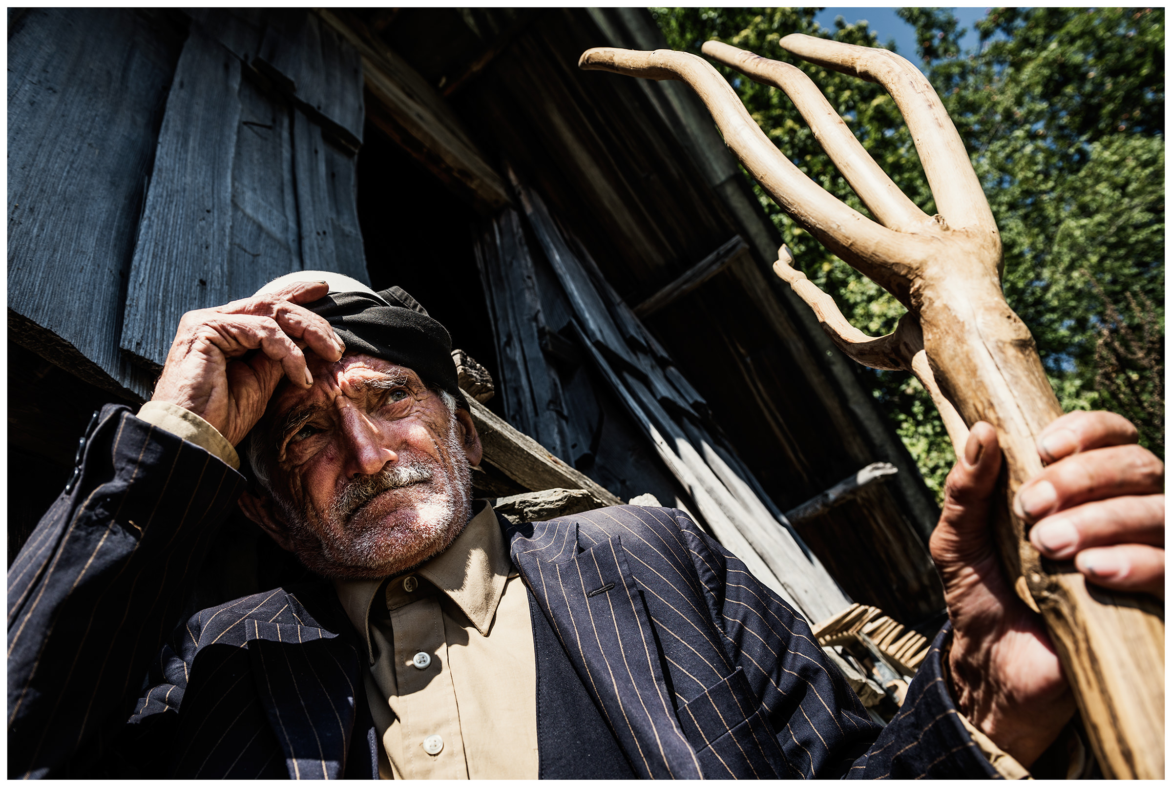 Cerem, Albania. An old man stands with a fork in his hand in front of a barn in the mountains.