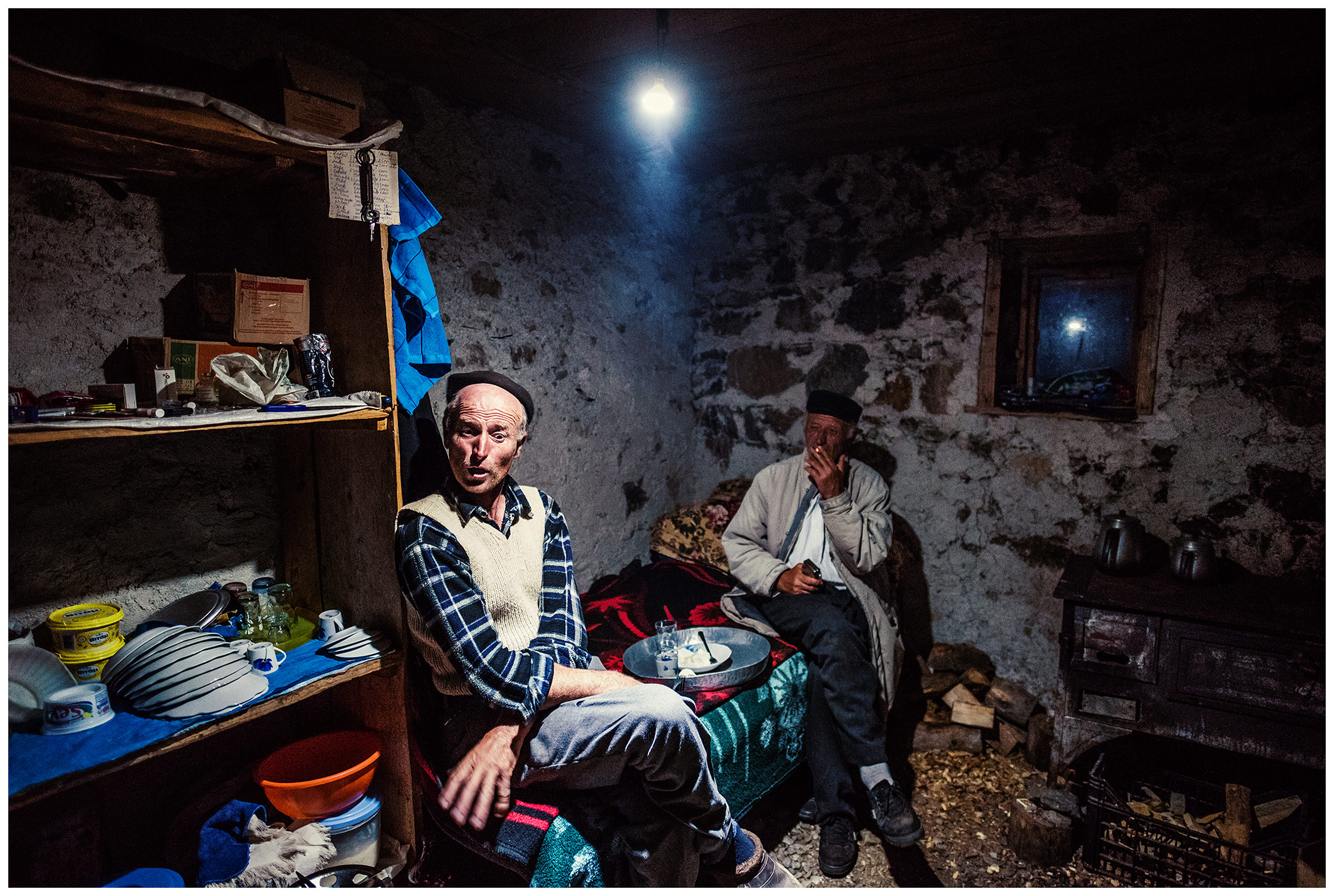 Doberdol, Albania. Two villagers sit on his bed and eat cheese with raki.