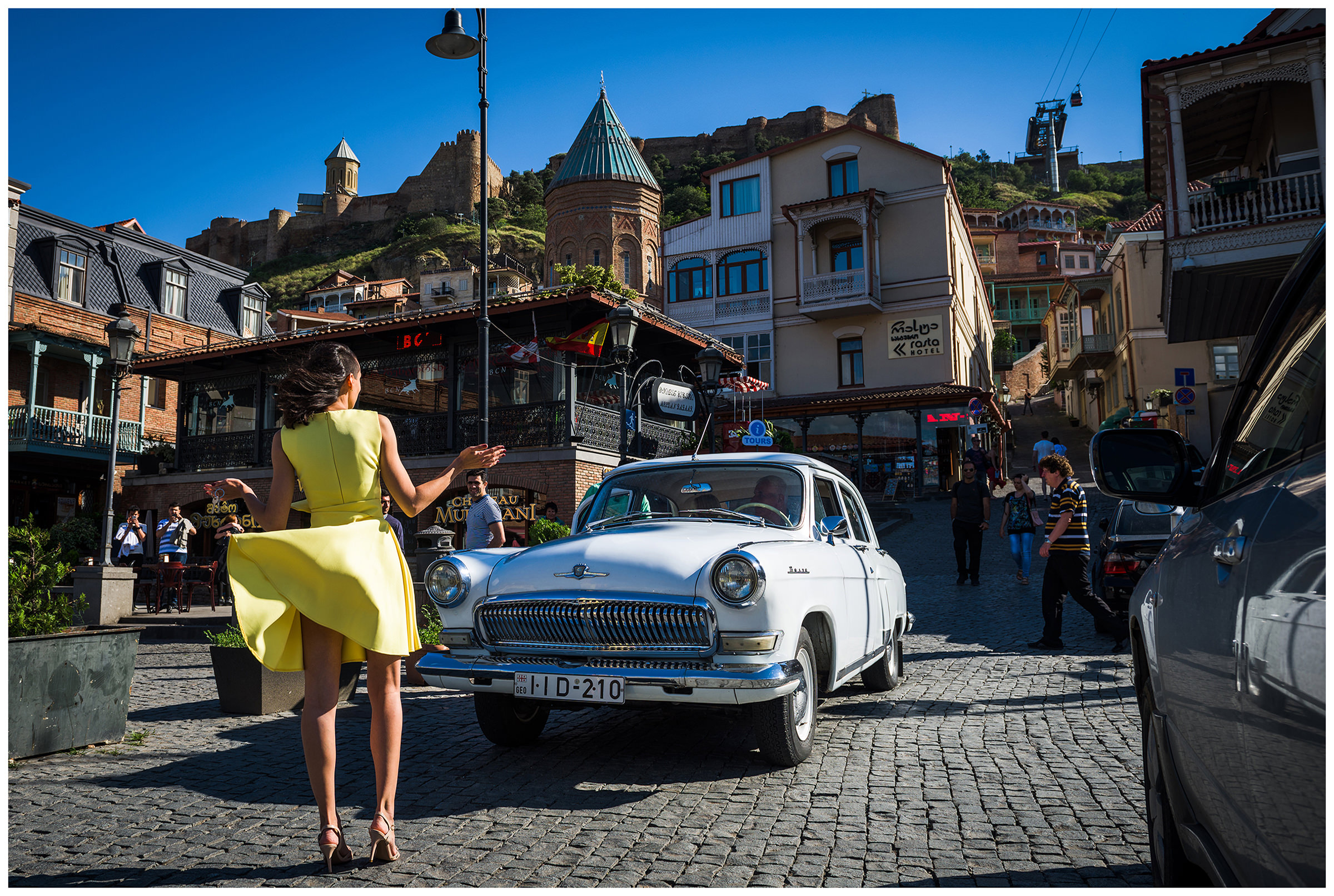 Georgia, Tbilisi. A woman in a yellow dress greets a man sitting in an old Soviet car Volga.