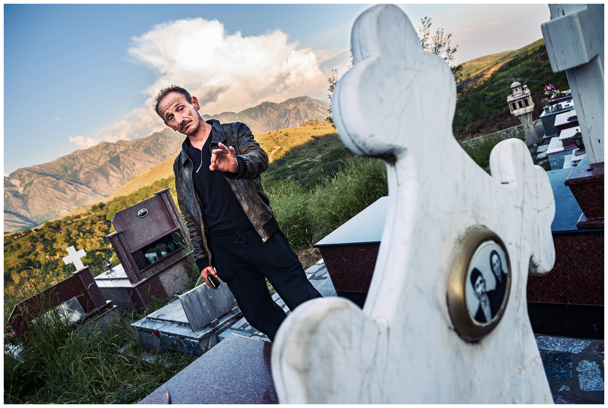 Albania, Pilur. A man stands in front of his parents' grave at the village cemetery.