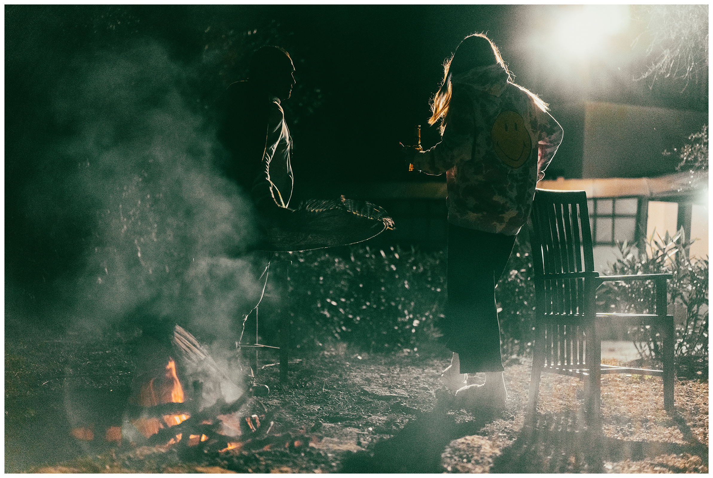 Miliou, Cyprus. A Israeli man and a woman with a bottle in their hands stand around a campfire in the Secret Forest wellness retreat late in the evening.