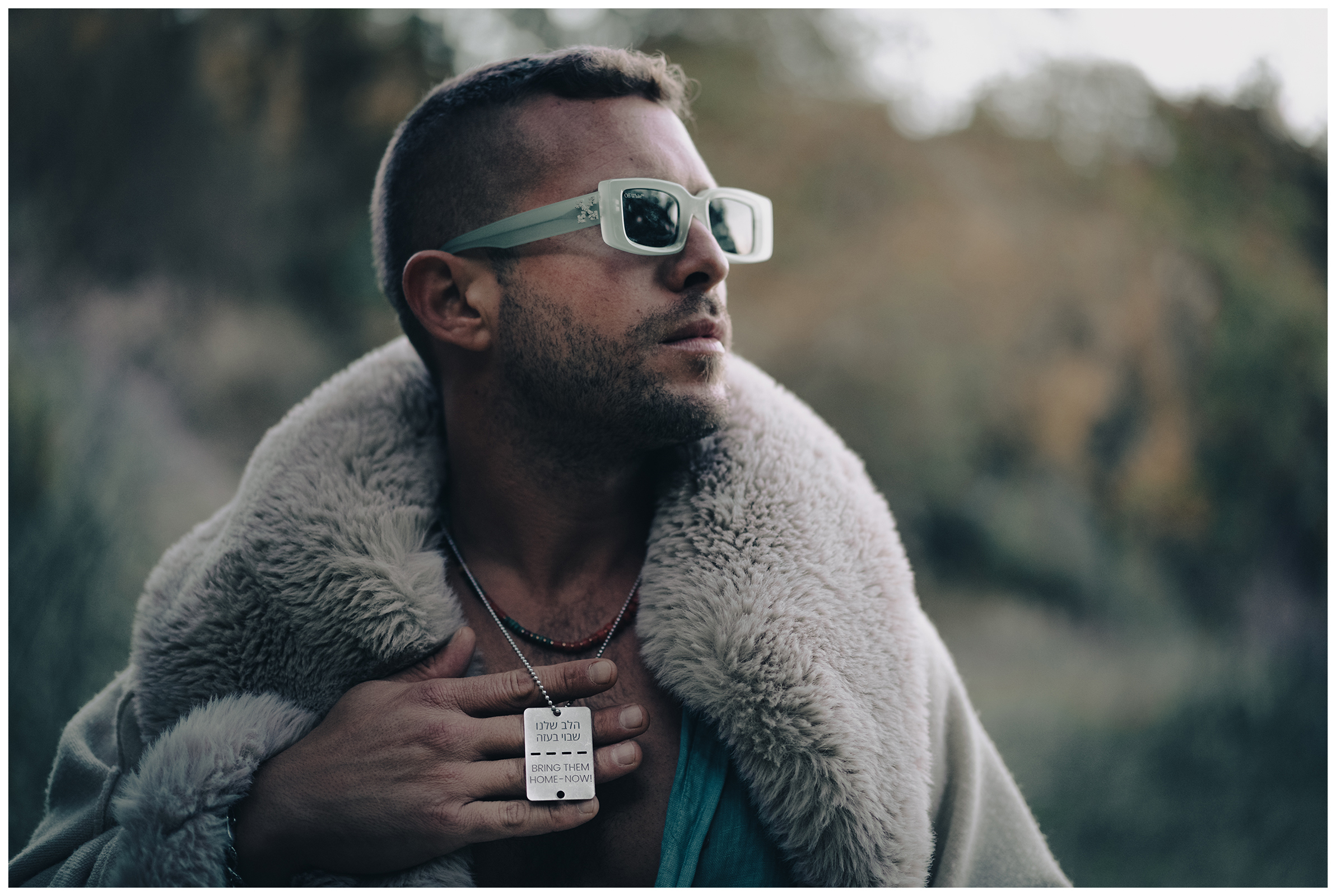 Miliou, Cyprus. A young Israeli man wearing sunglasses and a necklace with the inscription "Bring them home - now!" stands in a forest.