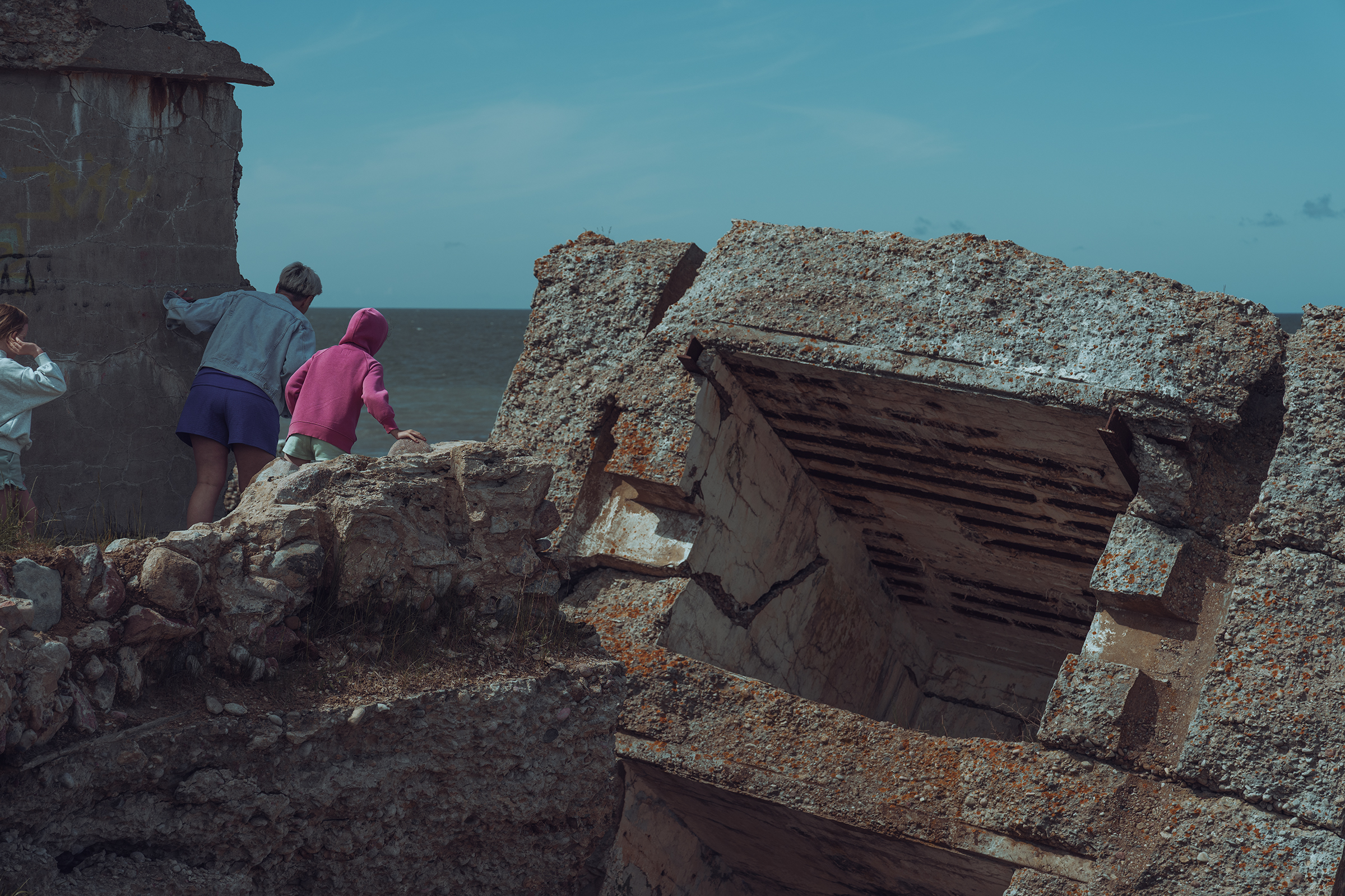 People explore the massive concrete ruins of an old military bunker collapsing into the sea on a beach in Latvia.